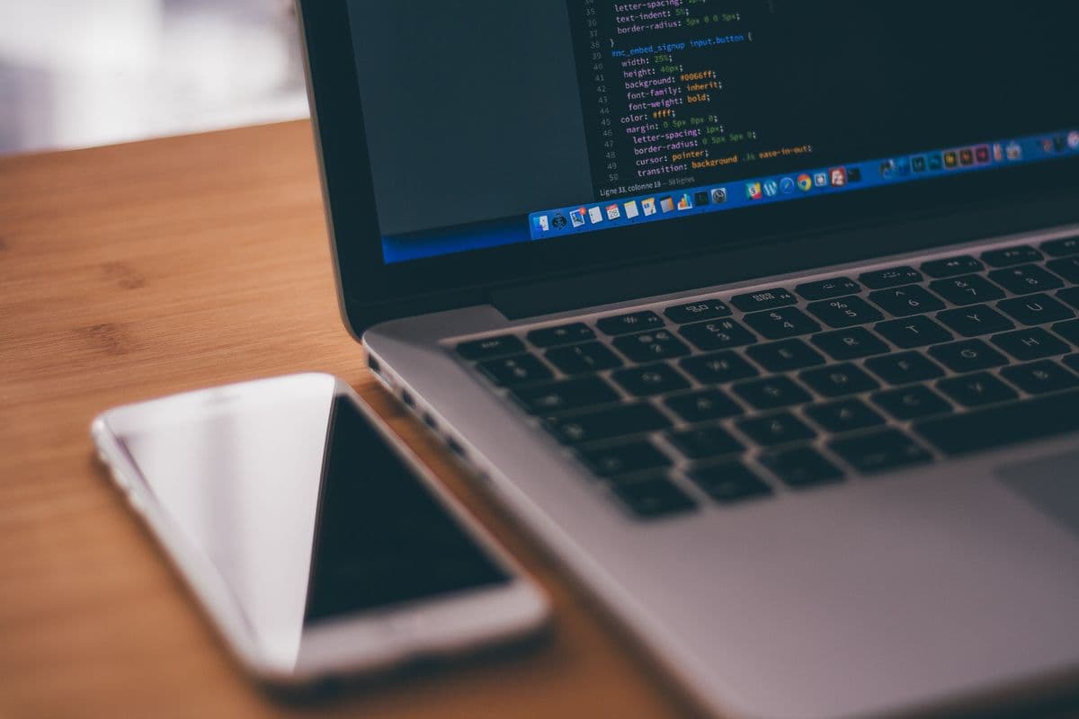A phone beside a laptop with code on screen