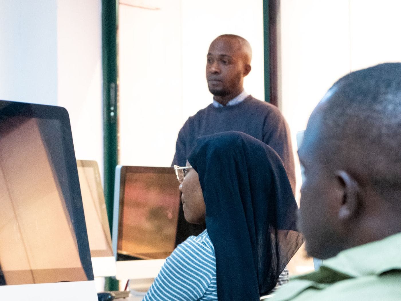 A trainer standing behind learners working at computers in a training room